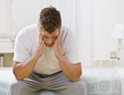 Stress and low mood A man sitting on a bed holding his head in his hands